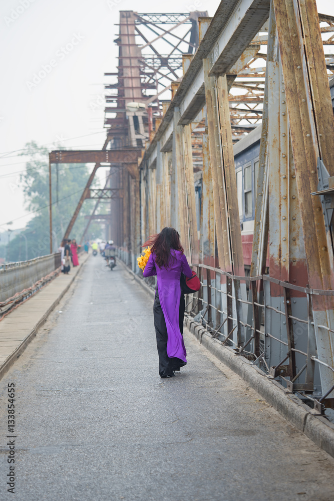 Vietnamese woman in traditional dress Ao Dai walking on old Long Bien bridge, Hanoi city