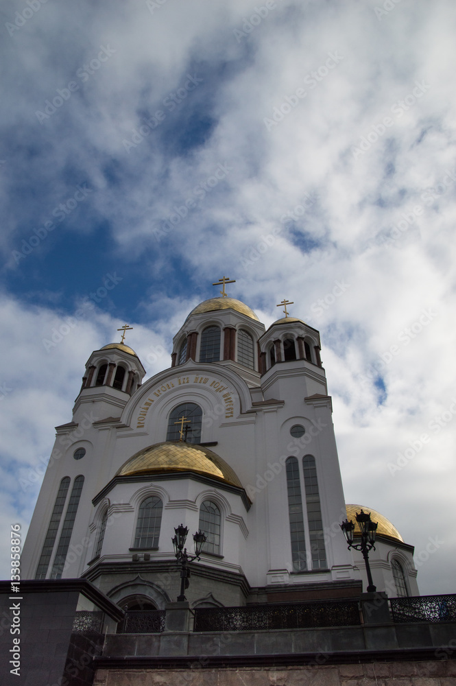 Obraz premium Church of All Saints, a Russian Orthodox Church built of the site of the Romanovs' execution in Yekaterinburg. The church has a white facade and golden onion domes topped with crosses.