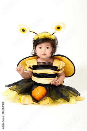 Baby girl dressed as cute little bee with a small pumpkin smiling