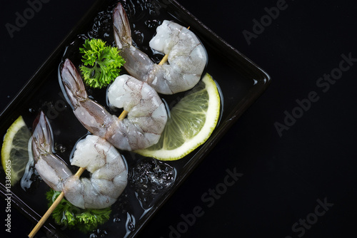 Raw shrimp with lemon on black plate black background