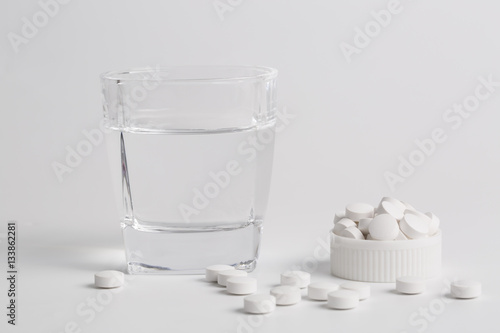 Round white pills and glass of water on a table. photo