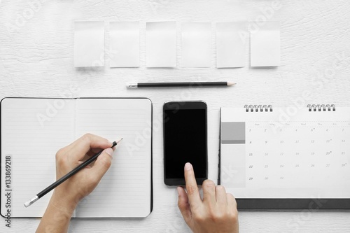 Hand  touch on a mobile phone black screen. , Hand-written in a notebook on a desk, top view. photo