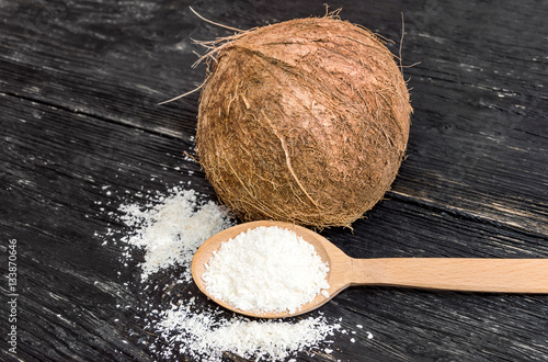 Coconut shaving in a wooden spoon and coconut on black wooden ta