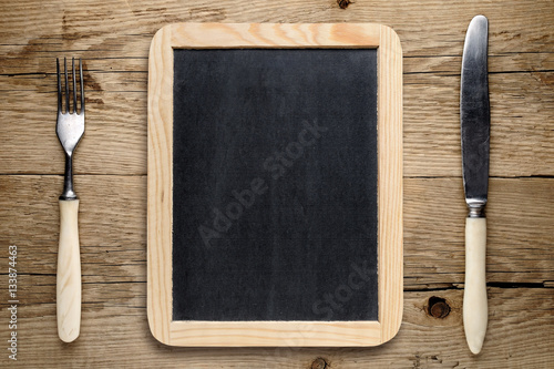 Blank blackboard, fork and knife on old wooden table