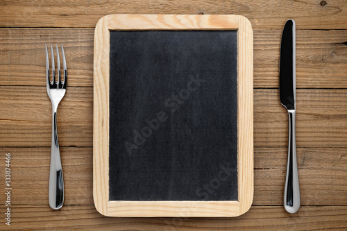 Blackboard for menu, fork and knife on wooden table