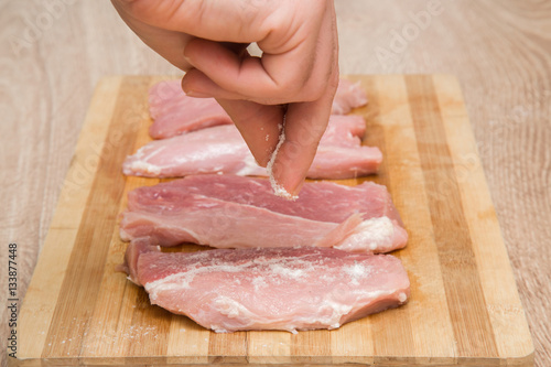 Man's fingers sprinkle salt on the meat on the wooden board in the kitchen. Cooking at home. Healthy eating and lifestyle.