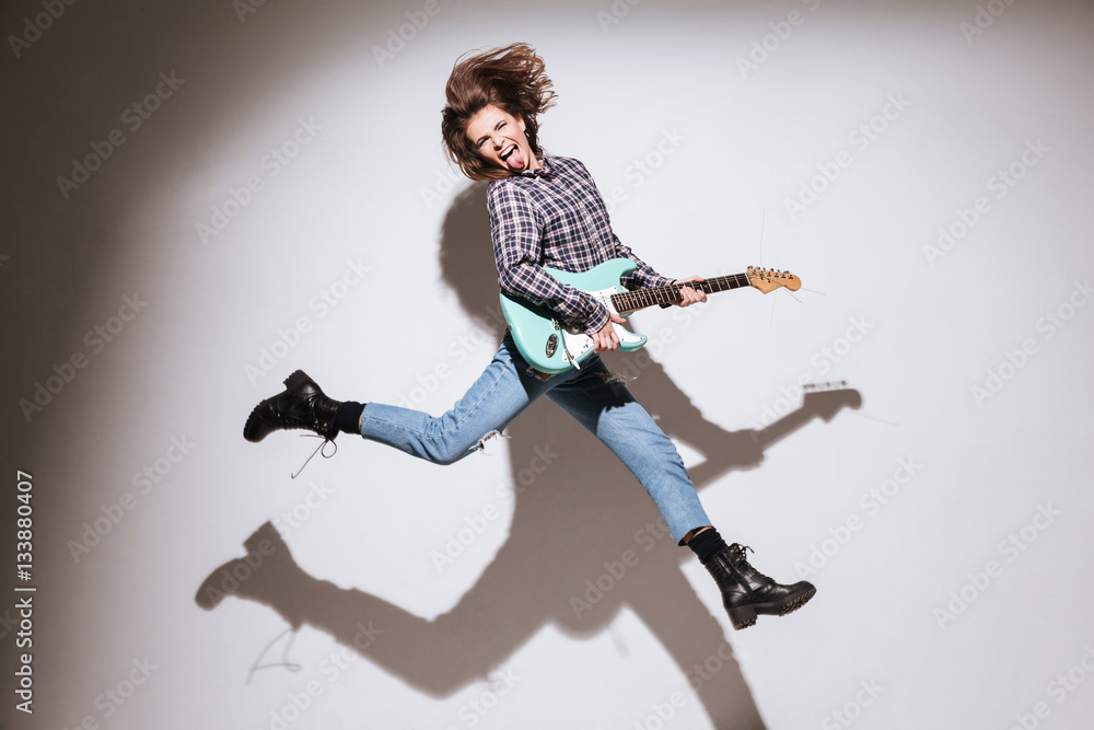 Emotional woman with guitar showing her tongue and jumping