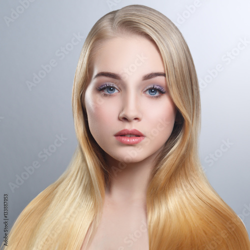 Beauty portrait of a cute blonde with long straight hair isolated groomed on a gray background.