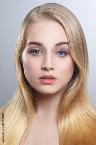 Beauty portrait of a cute blonde with long straight hair isolated groomed on a gray background.