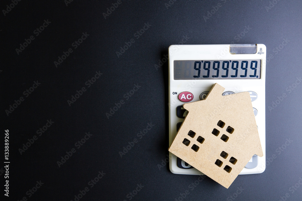 Wooden house toy and calculator on black background with copy sp Wooden house toy and calculator on black background with copy sp