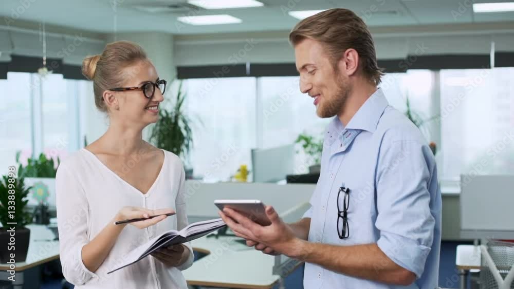 Two young successful colleagues discussing ideas at office . Man holding tablet, woman writing in notebook . Gesturing thumb up. Slow motion Two young successful colleagues discussing ideas at office . Man holding tablet, woman writing in notebook . Gesturing thumb up. Slow motion