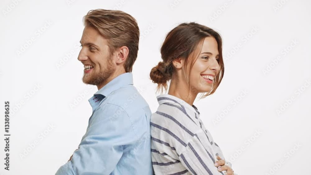 Beautiful Caucasian pair standing back to back flirtring laughing on white background in slowmotion Beautiful Caucasian pair standing back to back flirtring laughing on white background in slowmotion