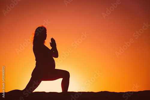 Silhouette of pregnant woman doing yoga on beach