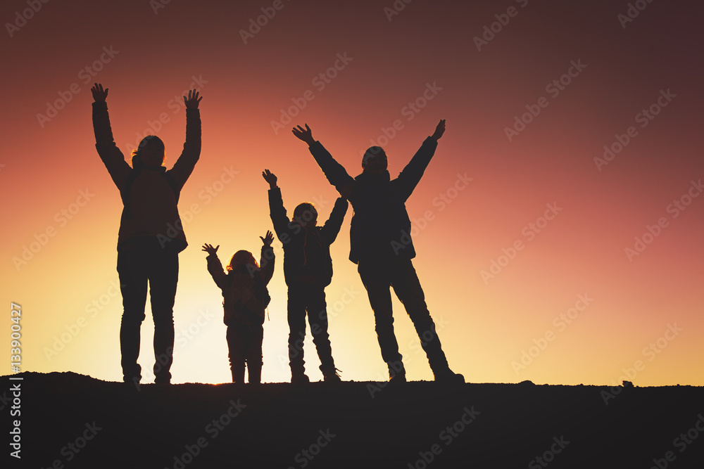 Silhouettes of happy family with two kids hiking at sunset