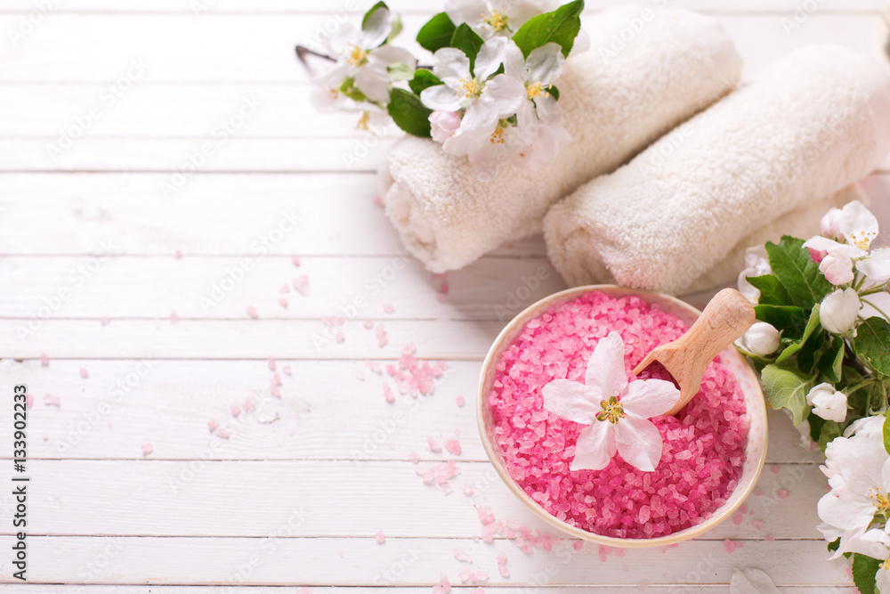 Pink sea salt in bowl, towels and flowers on white wooden backg Pink sea salt in bowl, towels and flowers on white wooden backg