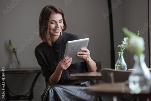 Beautiful woman sitting near window using tablet computer.