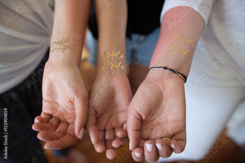 Three young women showing temporary 'Bride tribe' tattoos on wrists, close-up