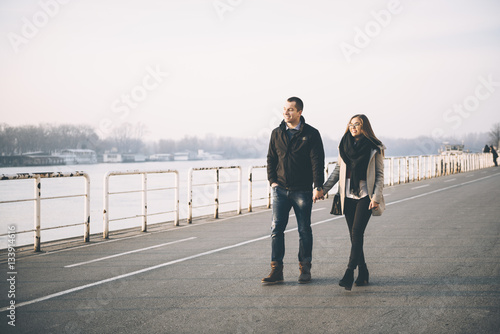 People in love theme. Attractive young couple enjoying in urban city outdoors. They walking by the river, holding hands and talking.