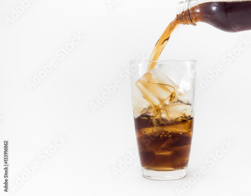 cola pouring from a plastic bottle into a glass filled with ice cubes