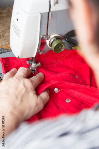 Older woman si fixing red jeans on a sewing machine.