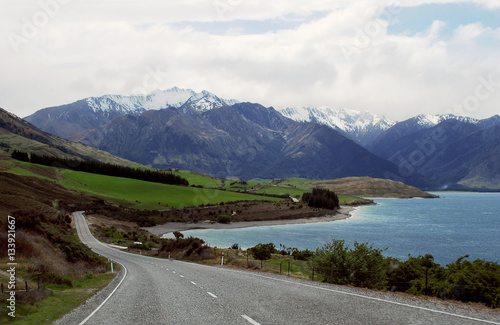 Scenic view panoramic of mount with snow cap and blue lake along long road in New Zealand.