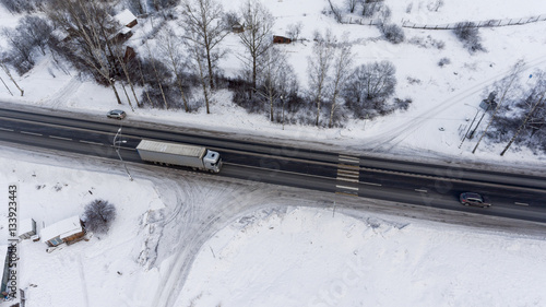 Freight semitrailer truck driving on the federal highway M10 at winter season. The Yazhelbitsy village, Novgorod district. Russia. Aerial view