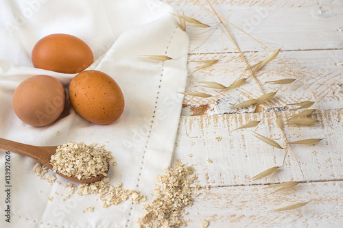 Brown eggs,dry oatmeal flakes on wooden spoon scattered over white linen cloth, wood background, healthy ingredients, mindful eating,beauty, skin care concept photo