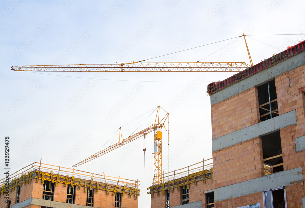 Construction industry and architecture - building new flats and houses, crane and derrick. Real property is unfinished - unplastered walls with visible bricks, cranes. Large area of sky