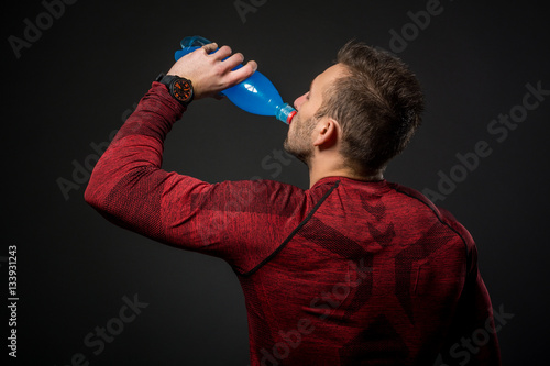 Young athletic man drinking energy drink after his exercising at gym