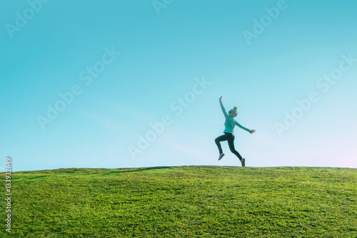 Alone asian Woman Jumping for Joy on a Grass Hill above horizon line One happy slim girl fly in a green field against blue summer sky with clouds Idea of success, growth , light, diet, luck, freedom