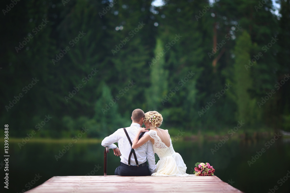 Beautiful young wedding couple sitting on the pier.