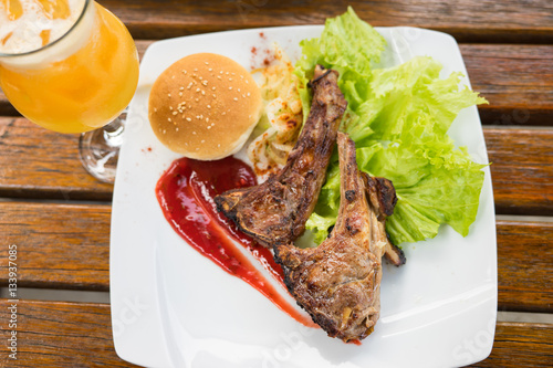 Grilled steak of lamb meat cut on slice with round bread, salad, oil, sauce and cup of orange juice