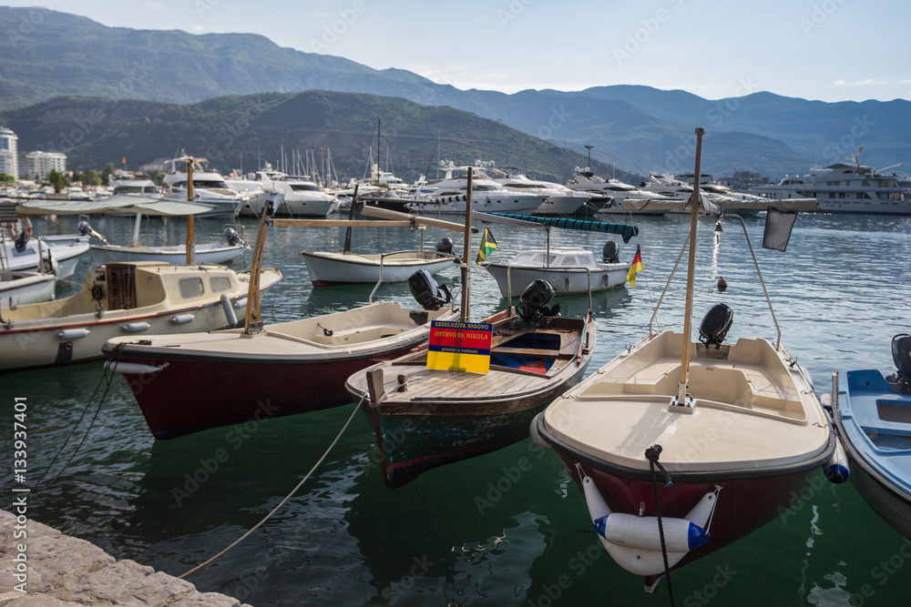 Old boats at the pier on the background of mountains and yachts.
