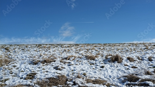 Partially snow covered hill and blue sky with some clouds