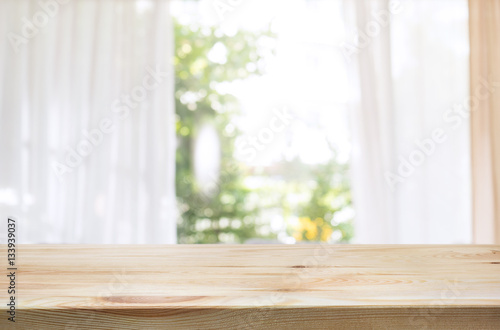 Wood table top on blur of curtain window and abstract green from garden background