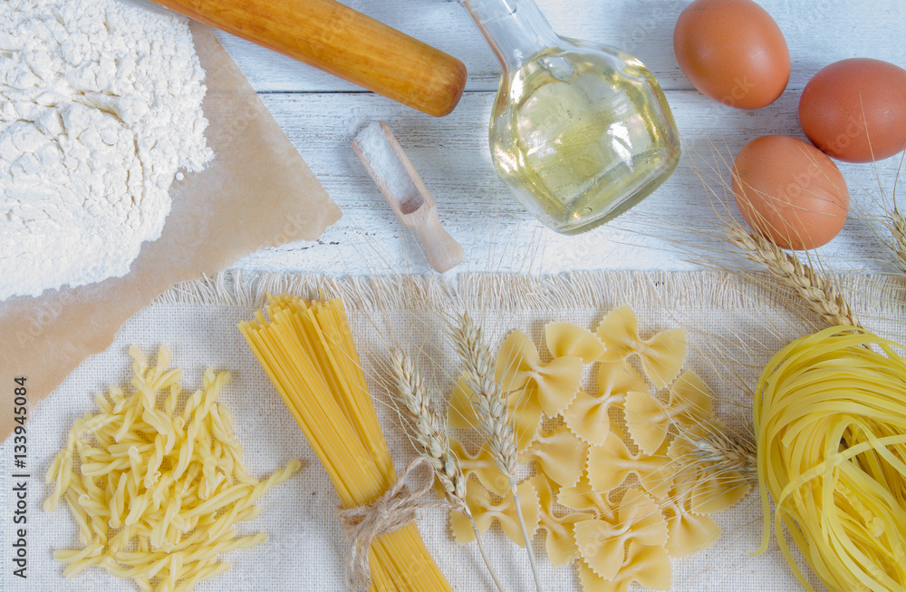 Pasta and wheat spikelets on a white wooden background