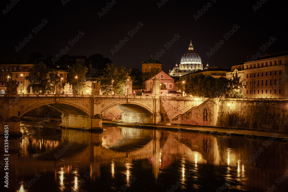 Basilica of San Pietro at night overlooking the Tevere river and surrounding historical landmarks of Rome.