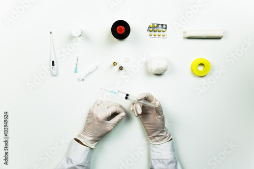 Medical doctor working place flat lay. Top view of hands of MD holding syringe ready for injection on table with medical utensils photo