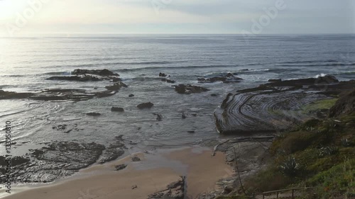 Natural amphitheater (stony curves) on Carriagem beach at low tide (Aljezur, Algarve, Portugal). Evening Atlantic coast landscape. Sometimes midges are flying before the camera.
