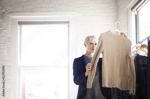 Young woman choosing clothes from rack at home