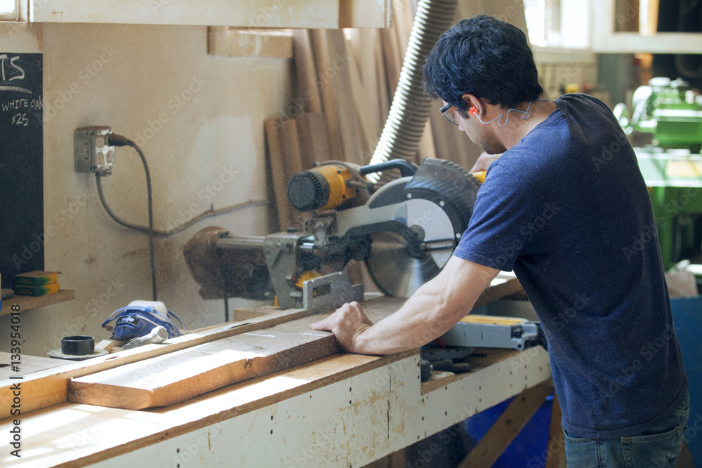 Side view of male carpenter cutting wooden plank with electric saw Side view of male carpenter cutting wooden plank with electric saw