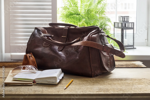 Leather bag and books on table at home office by window
