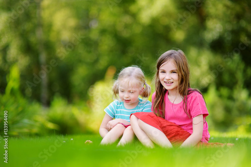 Two cute little sisters having fun together on the grass on summer day