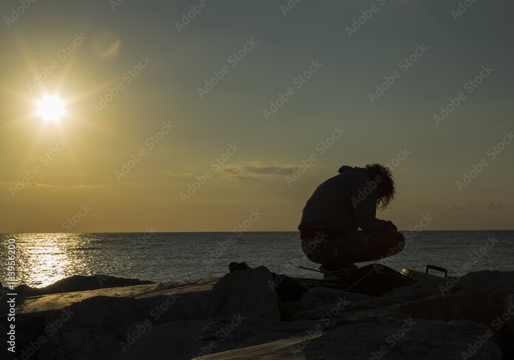 Man fishing in first rays of sunlight on sea shore
