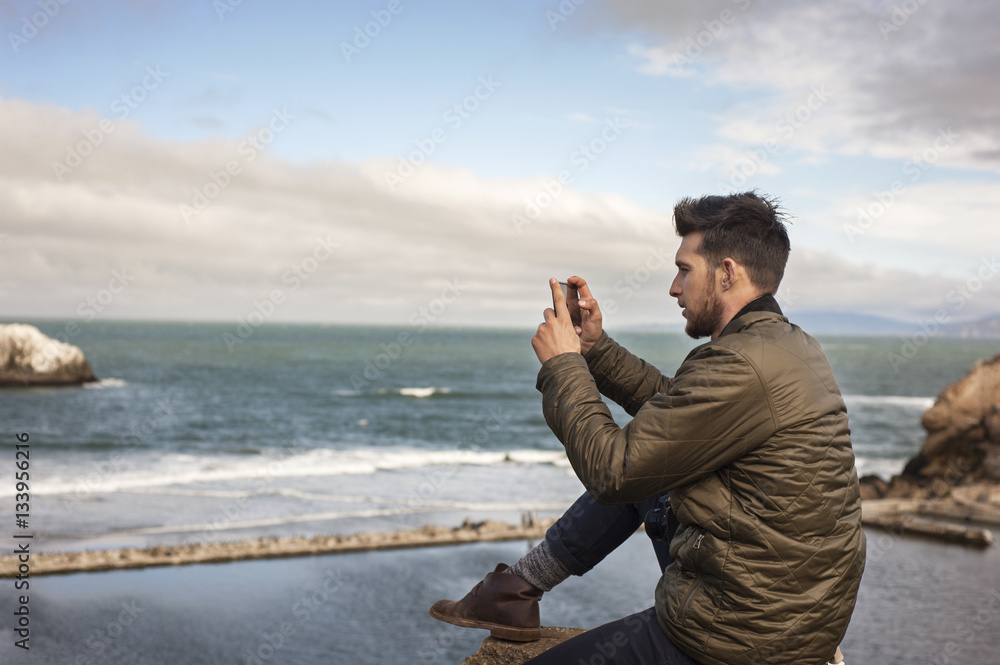 Side view of man taking picture of sea through smartphone Side view of man taking picture of sea through smartphone