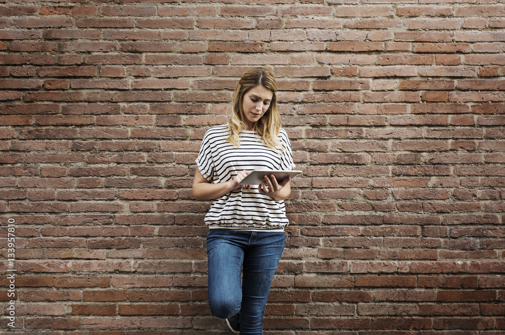Woman using tablet computer while standing against brick wall Woman using tablet computer while standing against brick wall