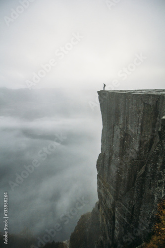 Distant view of person standing on cliff against cloudy sky