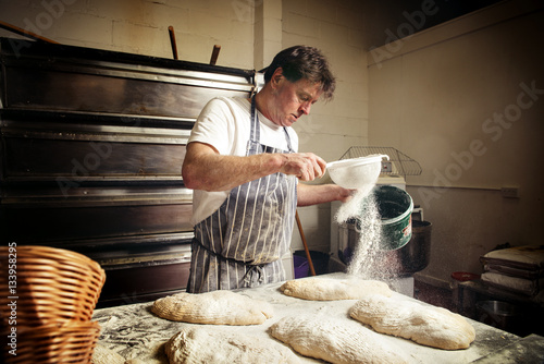 Male baker sprinkling flour on bread dough at bakery photo
