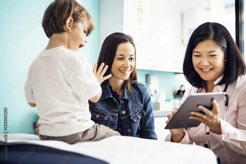 Happy doctor using tablet computer with family in clinic Happy doctor using tablet computer with family in clinic