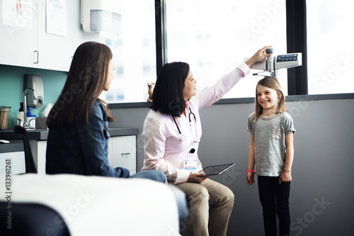 Female doctor measuring girl's height while mother sitting at clinic photo